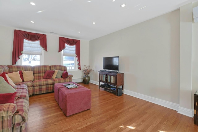 living room featuring a wall unit AC, recessed lighting, visible vents, light wood-style floors, and baseboards