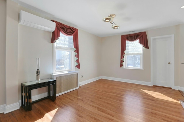 interior space featuring radiator, an AC wall unit, a healthy amount of sunlight, and wood finished floors