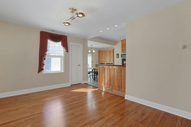 unfurnished living room featuring a notable chandelier, recessed lighting, light wood-type flooring, and baseboards