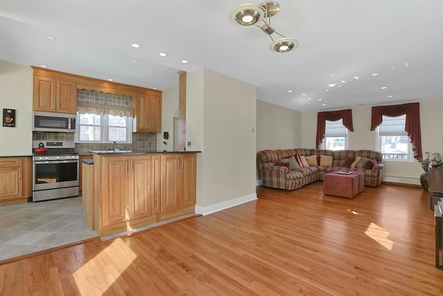 kitchen featuring open floor plan, appliances with stainless steel finishes, light wood finished floors, dark countertops, and tasteful backsplash