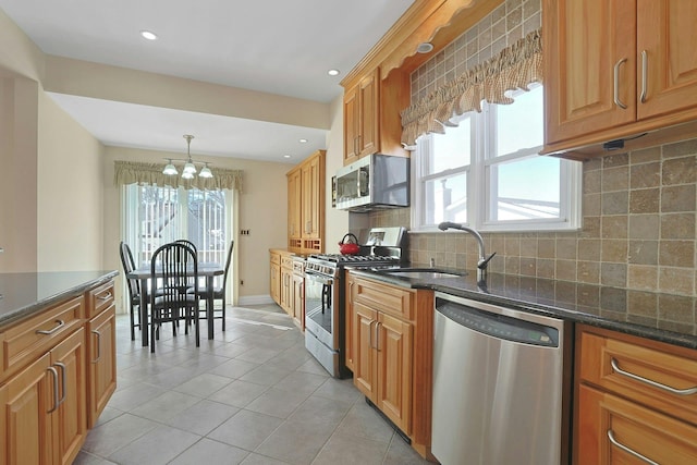 kitchen with a sink, appliances with stainless steel finishes, brown cabinets, dark stone countertops, and decorative light fixtures