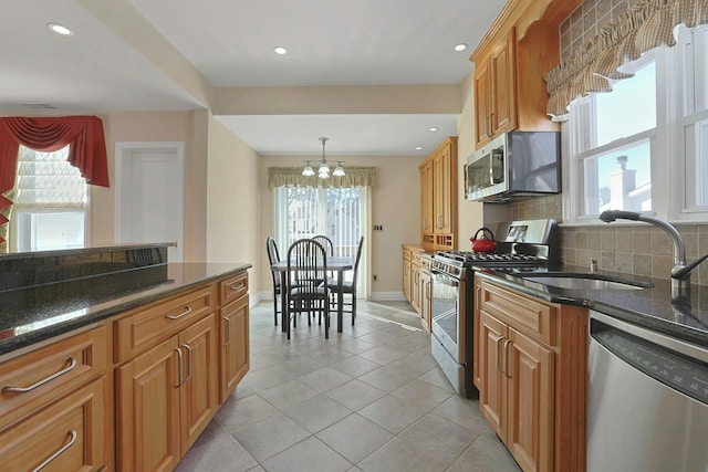 kitchen featuring stainless steel appliances, hanging light fixtures, backsplash, a sink, and dark stone counters