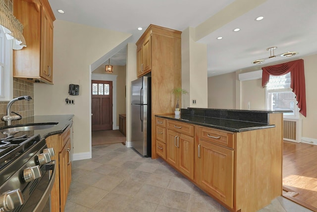 kitchen featuring decorative backsplash, appliances with stainless steel finishes, a healthy amount of sunlight, a sink, and dark stone counters