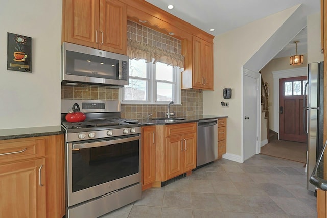 kitchen featuring brown cabinets, stainless steel appliances, decorative backsplash, a sink, and dark stone countertops