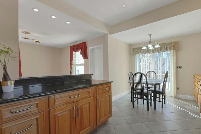 kitchen with brown cabinets, decorative light fixtures, light tile patterned floors, dark stone counters, and baseboards