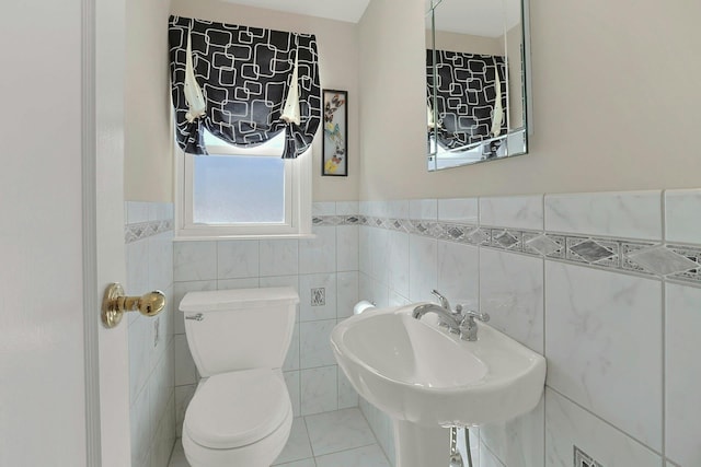 half bathroom with a wainscoted wall, a sink, tile walls, and toilet