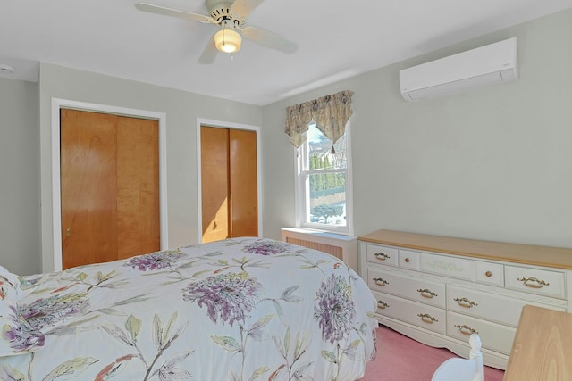 bedroom with a wall unit AC, two closets, radiator, and a ceiling fan