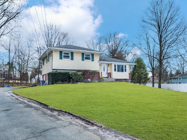 split level home featuring brick siding, a chimney, a front yard, fence, and driveway