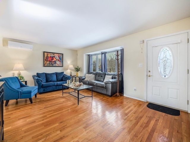 living room with baseboards, a wall unit AC, and light wood finished floors