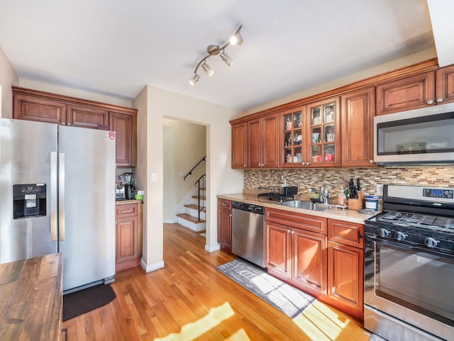 kitchen featuring stainless steel appliances, butcher block countertops, a sink, backsplash, and glass insert cabinets