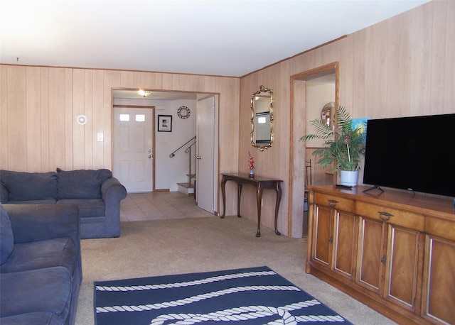 living area featuring stairs, wooden walls, and light colored carpet