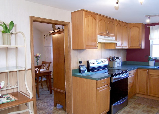 kitchen with dark countertops, electric stove, rail lighting, and under cabinet range hood