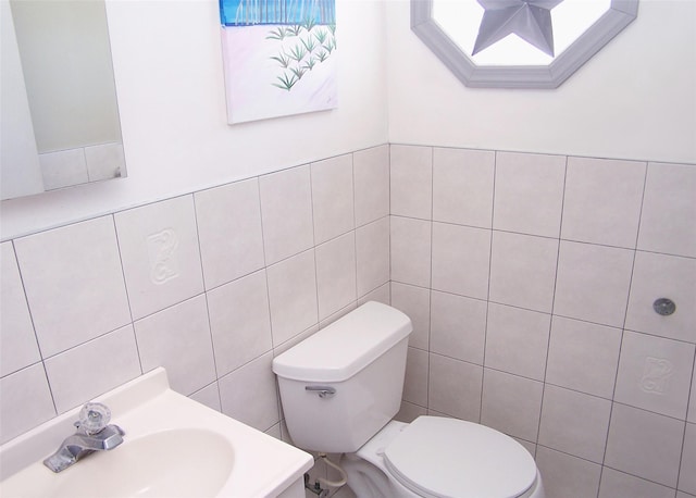 half bathroom with a sink, tile walls, and toilet