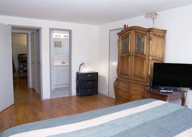 bedroom with light wood-type flooring, a sink, and connected bathroom