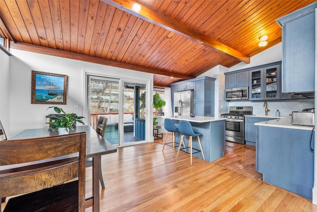 kitchen with light wood-style flooring, glass insert cabinets, stainless steel appliances, light countertops, and a kitchen bar