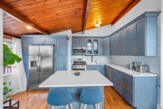 kitchen featuring lofted ceiling with beams, a kitchen breakfast bar, appliances with stainless steel finishes, tasteful backsplash, and glass insert cabinets