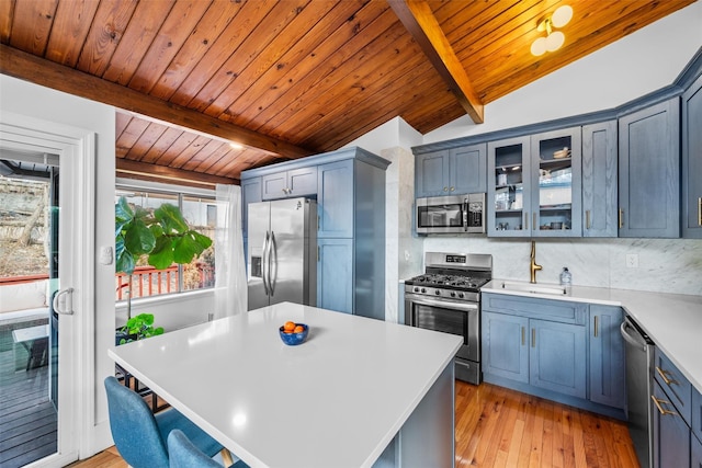 kitchen with vaulted ceiling with beams, light wood-style flooring, stainless steel appliances, light countertops, and decorative backsplash