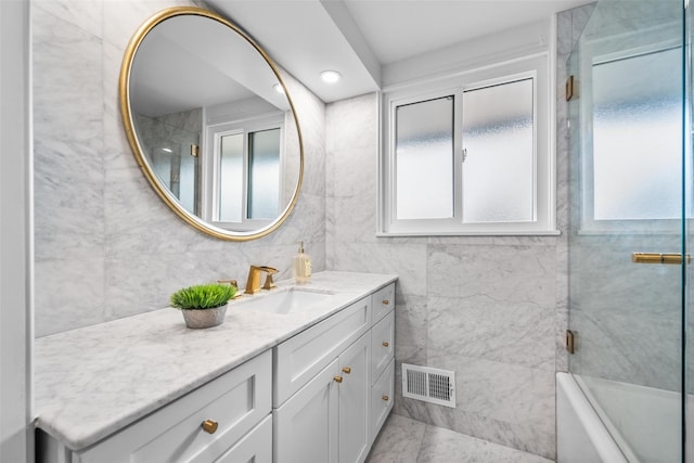 full bathroom with tile walls, visible vents, plenty of natural light, and vanity