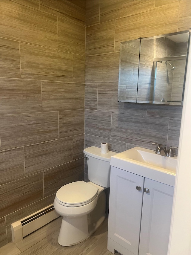 full bath featuring toilet, vanity, tile walls, baseboard heating, and a tile shower