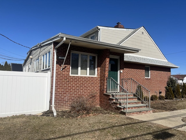 bungalow featuring brick siding, fence, a chimney, and roof with shingles