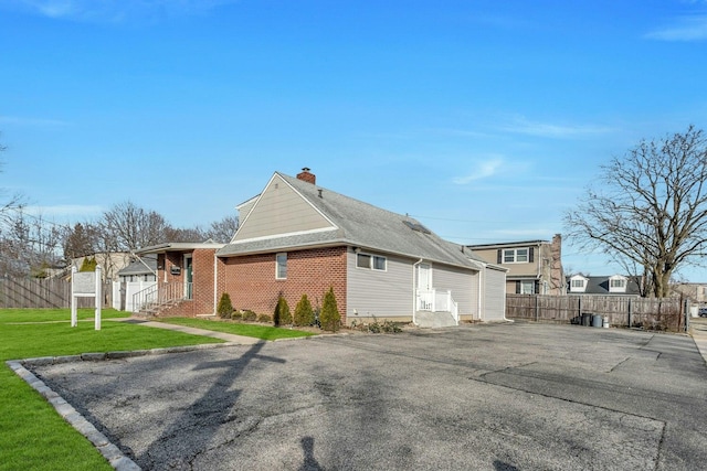 view of home's exterior with fence, a chimney, entry steps, aphalt driveway, and a lawn