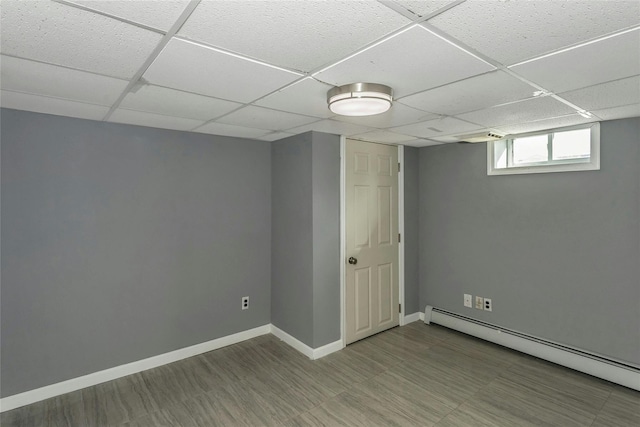 basement featuring a drop ceiling, baseboards, and baseboard heating