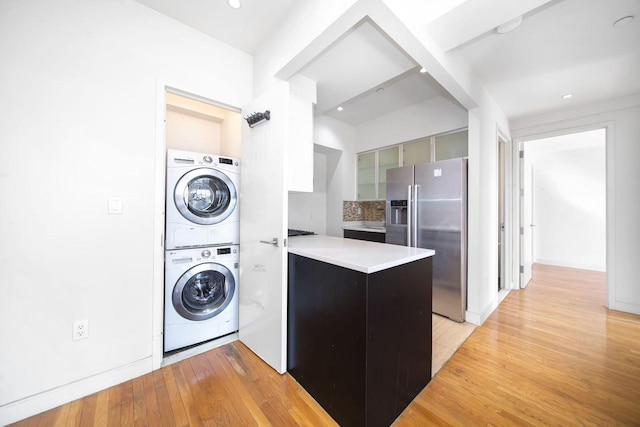 clothes washing area featuring laundry area, stacked washing maching and dryer, and light wood-style floors