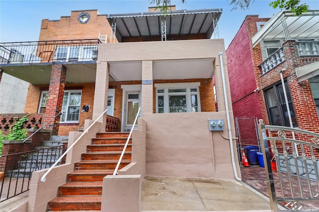 view of front of house featuring a balcony, brick siding, fence, stairs, and a gate