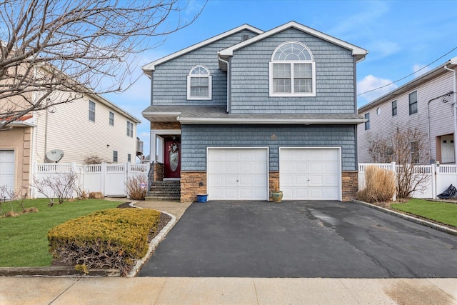 view of front of home with stone siding, an attached garage, fence, and driveway