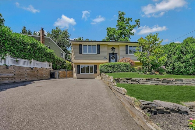 raised ranch with driveway, a front lawn, and fence