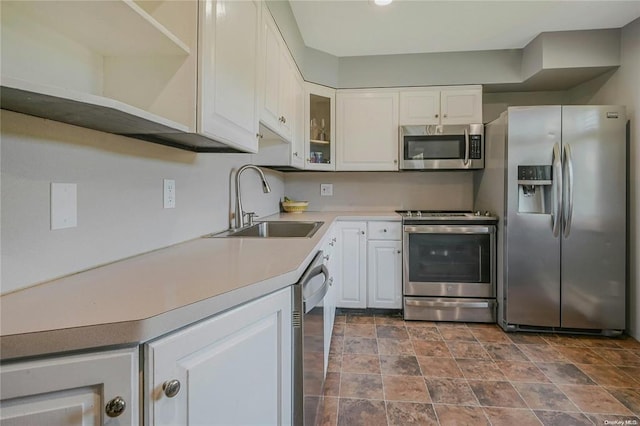 kitchen featuring stainless steel appliances, light countertops, glass insert cabinets, white cabinets, and a sink