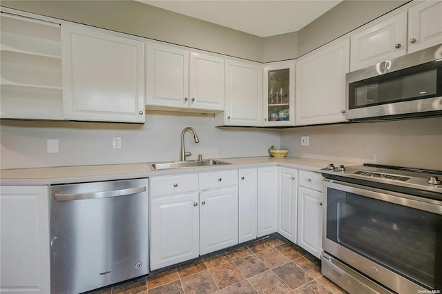 kitchen featuring stainless steel appliances, a sink, white cabinetry, light countertops, and glass insert cabinets