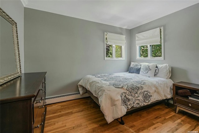 bedroom with ornamental molding, baseboard heating, and wood finished floors