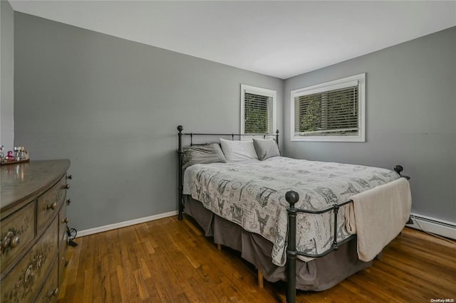 bedroom featuring a baseboard heating unit, baseboards, and dark wood-type flooring