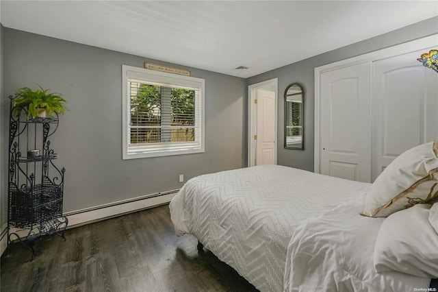 bedroom featuring a baseboard heating unit, a closet, and dark wood finished floors