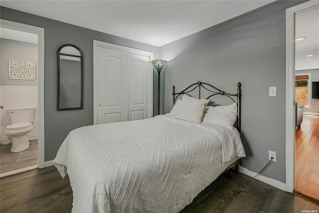 bedroom with dark wood finished floors, tile walls, a closet, connected bathroom, and baseboards