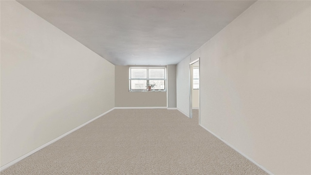 spare room featuring light carpet and baseboards