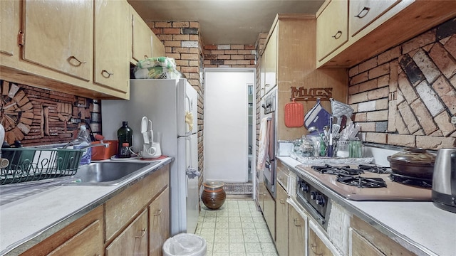 kitchen featuring brick wall, freestanding refrigerator, light countertops, light floors, and gas stovetop