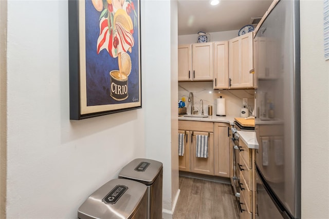 kitchen featuring light wood-style flooring, a sink, light countertops, light brown cabinetry, and tasteful backsplash