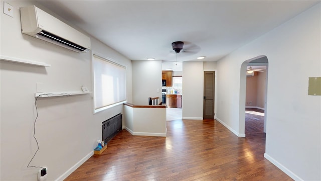 interior space featuring arched walkways, a ceiling fan, radiator, hardwood / wood-style flooring, and a wall mounted AC