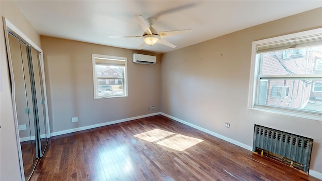 unfurnished bedroom with radiator, a wall mounted air conditioner, baseboards, and wood finished floors