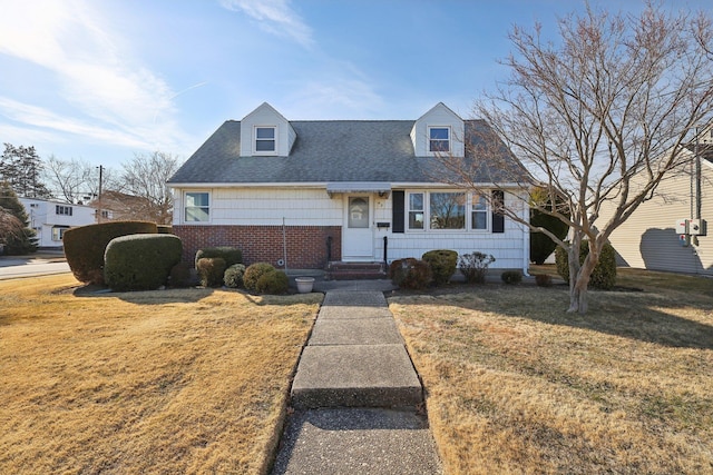 new england style home with a shingled roof, a front yard, and brick siding