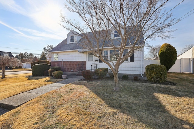 cape cod house featuring brick siding, a front yard, and fence