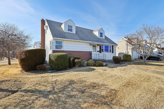 new england style home featuring roof with shingles, brick siding, a chimney, and a front yard