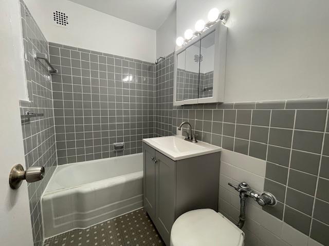 bathroom featuring shower / bath combination, toilet, tile walls, and vanity