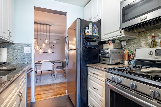 kitchen with stainless steel appliances, white cabinetry, ornamental molding, backsplash, and dark stone counters