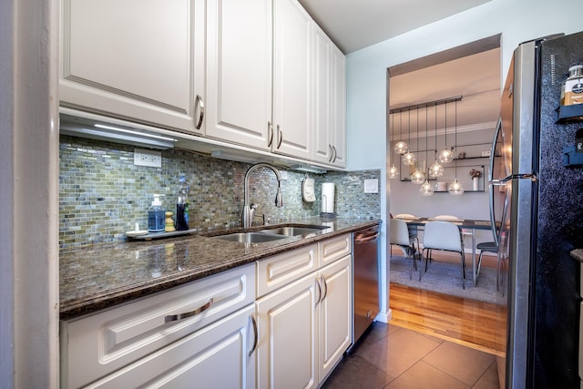 kitchen featuring stainless steel appliances, white cabinetry, a sink, and dark stone countertops