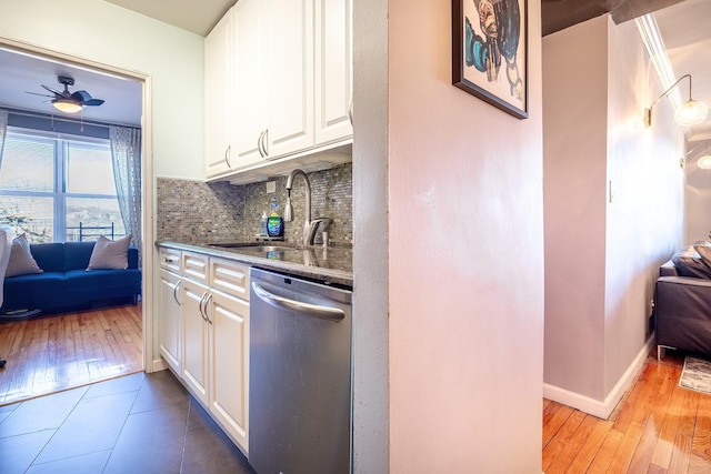 kitchen featuring a sink, white cabinetry, stainless steel dishwasher, tasteful backsplash, and dark stone countertops