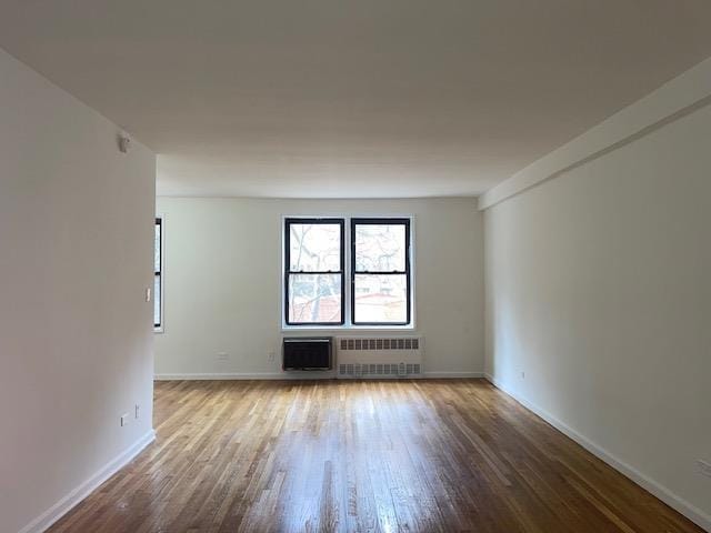 spare room featuring radiator heating unit, baseboards, and wood finished floors