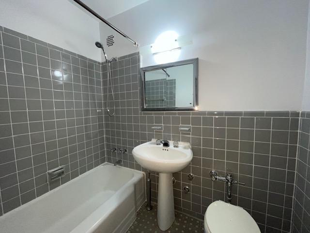 bathroom with toilet, tile patterned flooring, tile walls, and shower / bathing tub combination